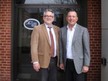 Interim ECU President Dr. Jeffrey Gibson, left, and Oka' Institute Executive Director Duane Smith pose in front of the Oka' Institute offices. The Oka' Institute logo shows over Gibson's shoulder