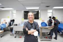 East Central University Nursing student Matison Worcester stands inside a nursing simulation lab while fellow students work in the background.